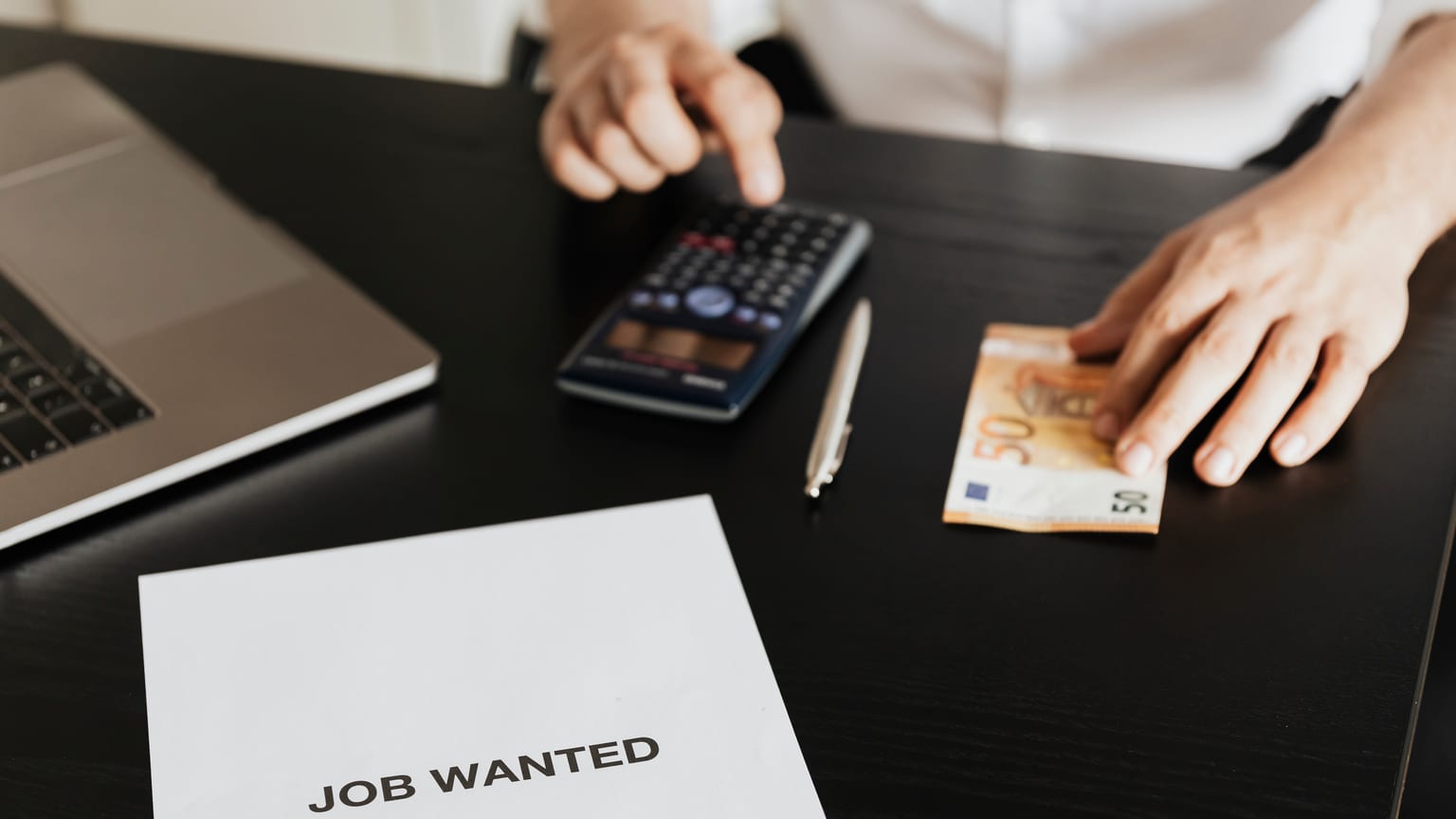 Muž počítá na kalkulačce u listu Job Wanted — nárok na odstupné po ztrátě zaměstnání